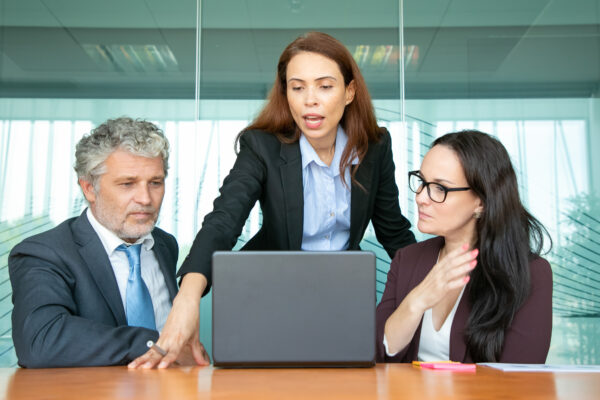 Confident project manager showing presentation to colleagues. Businesswoman standing at open laptop in meeting room, speaking and explaining content details to partners. Communication concept, Salesforce Marketing Training