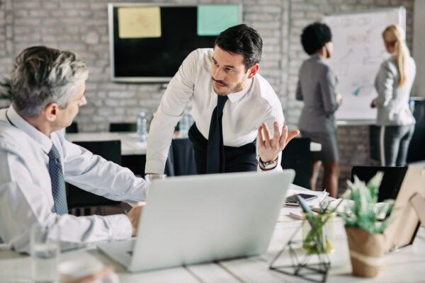 Young serious businessman talking to his male colleague in the office. There are people working in the background, Salesforce Marketing Training