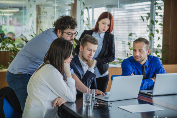 Team of professionals collaborating around laptops in a modern office, discussing data and strategy — concept of team-based Salesforce training program and digital workplace solutions, Salesforce Training Program